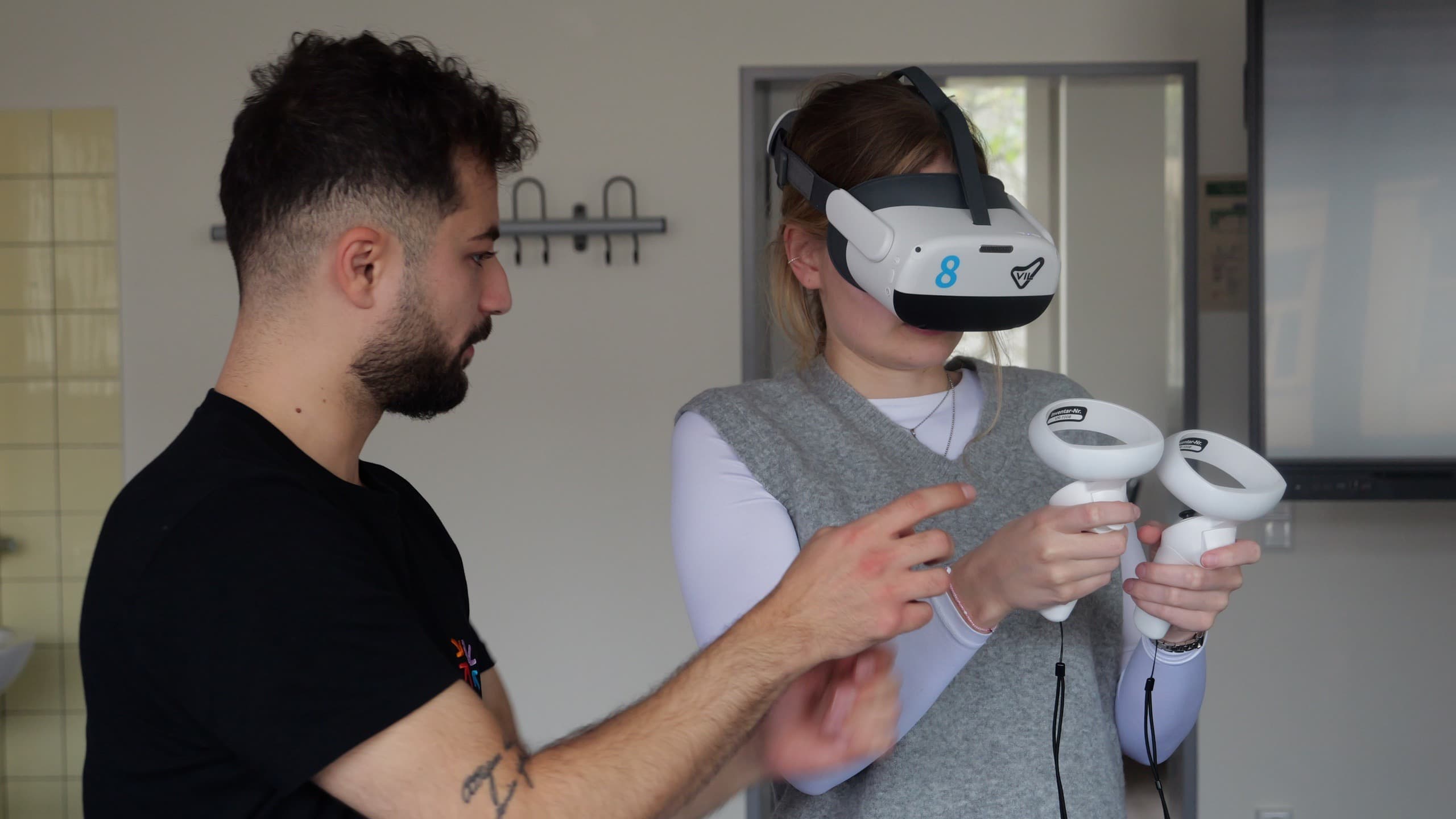 Eine junge Person trägt eine Virtual-Reality-Brille und wird dabei von einem GAMESHIFT-Mitarbeiter begleitet.