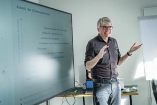 Workshop-Leiter präsentiert vor einer Folie zum Entstehungsprozess.